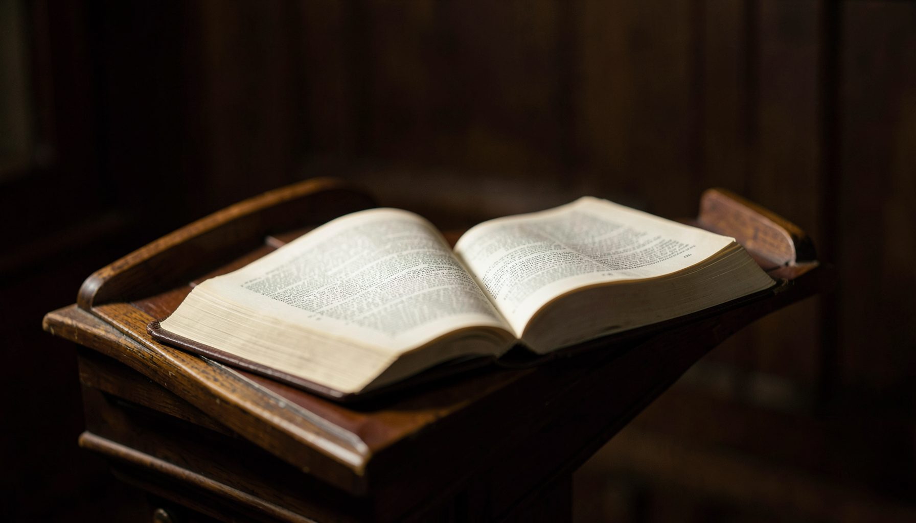 An open Bible resting on a wooden lectern in soft, warm light, with deep browns and muted gold tones creating a reverent atmosphere