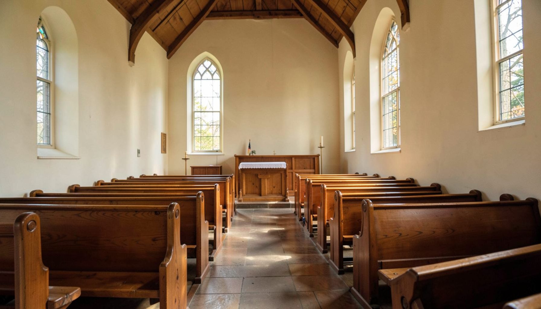 Interior of a simple church sanctuary with warm wooden pews and soft natural light filtering through windows, peaceful atmosphere