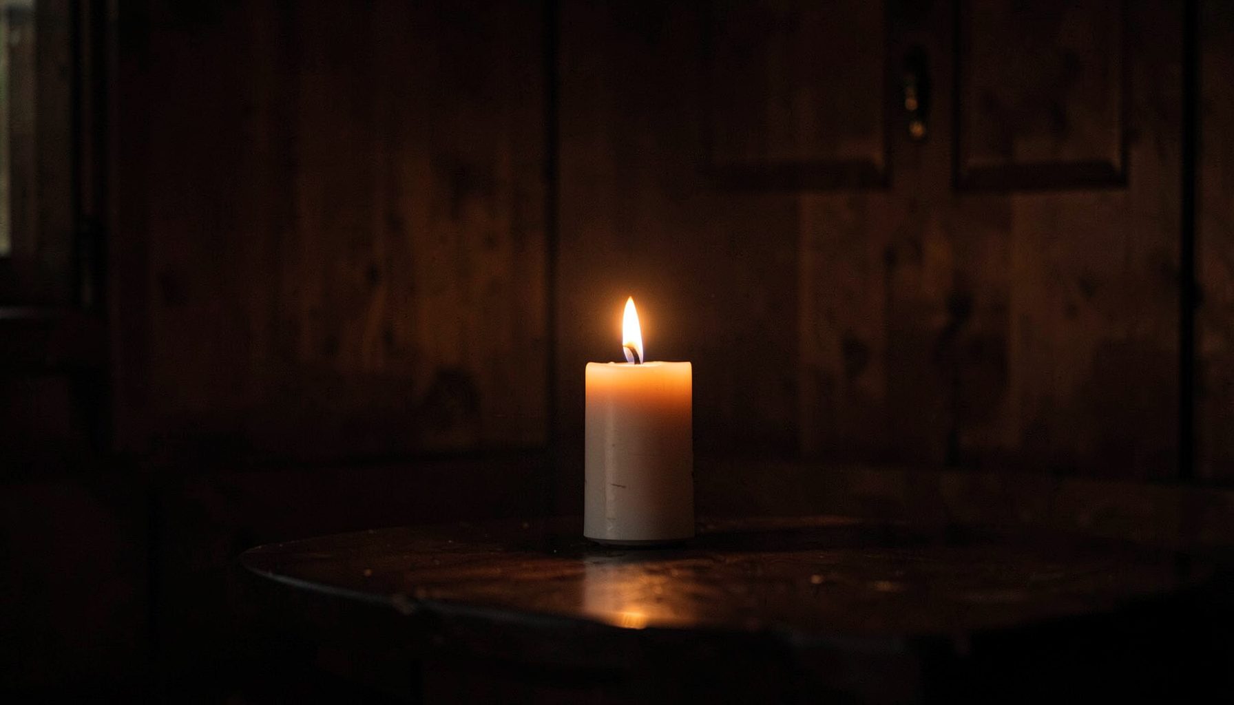 Warm candlelight glowing against a dark wood interior, soft amber and deep brown tones, quiet reverent atmosphere